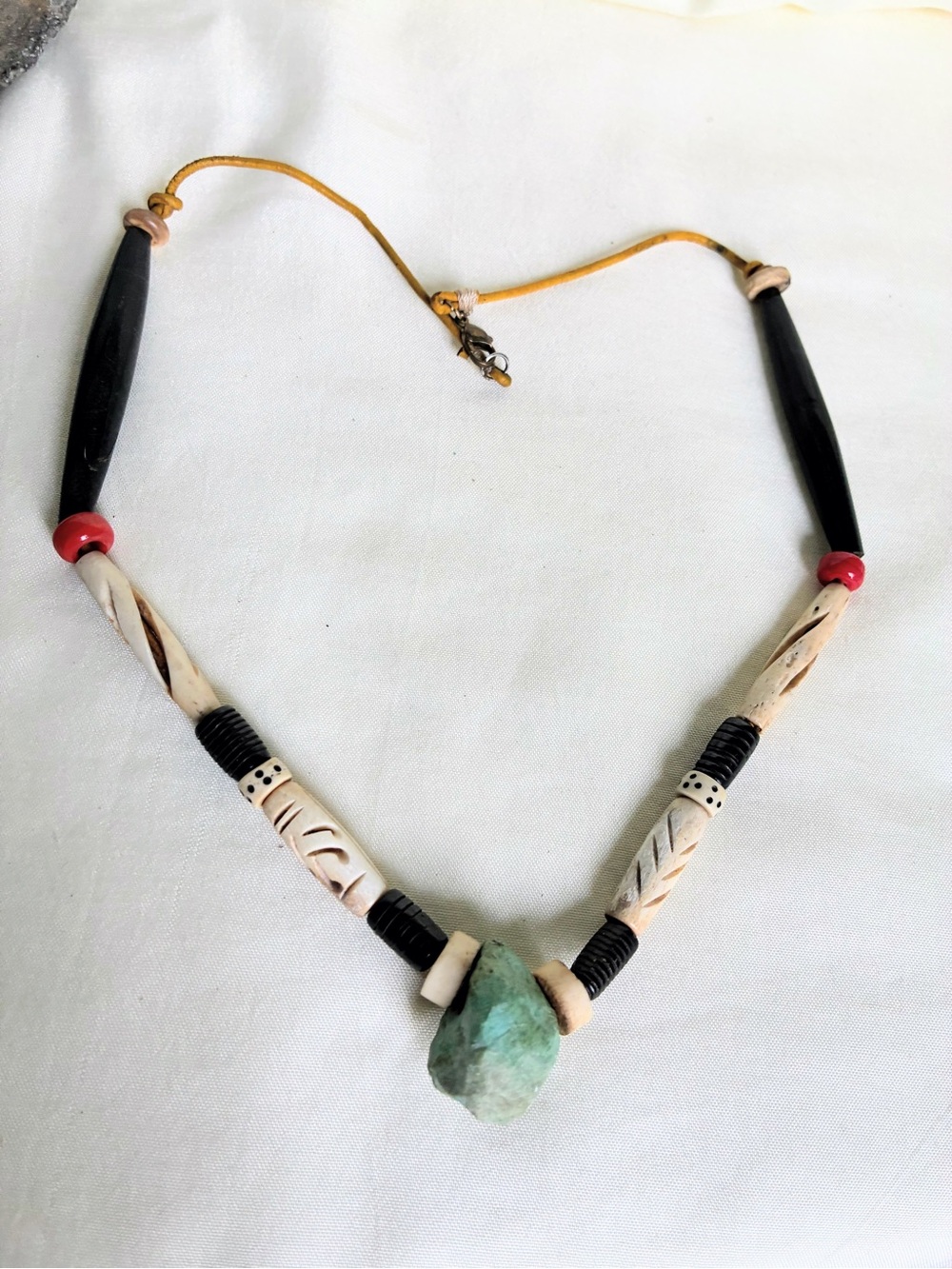 Handmade necklace with carved bone beads, black beads, red beads, and a green